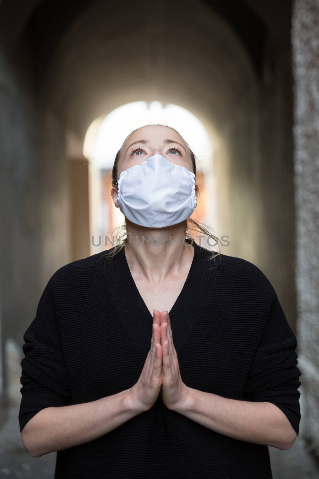 Coronavirus outbreak. Young caucasian woman wearing medical protection face mask praying over coronavirus global pandemic, for salvation of humanity, health, anxiety and depression reduction by kasto