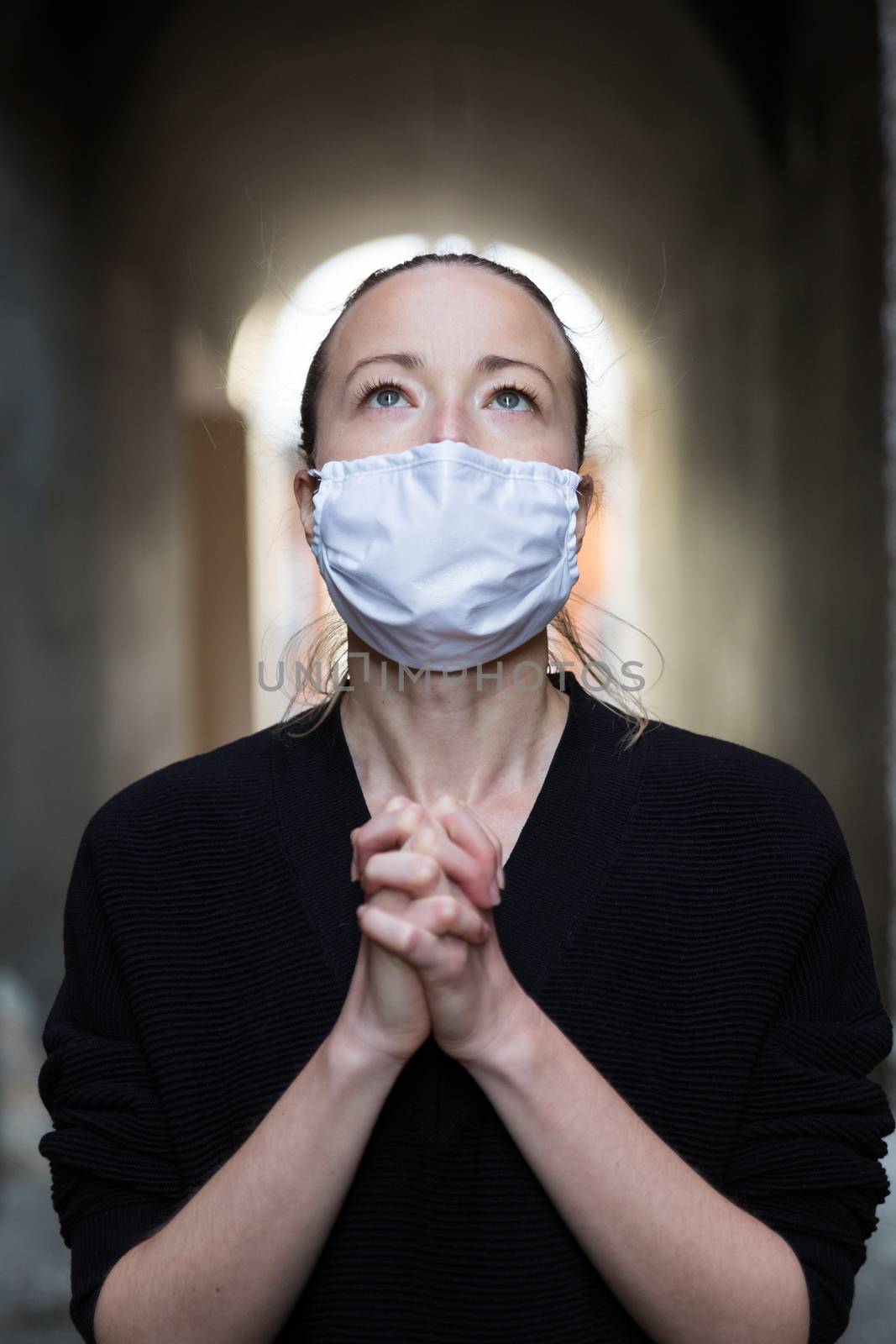 Coronavirus outbreak. Young caucasian woman wearing medical protection face mask praying over coronavirus global pandemic, for salvation of humanity, health, anxiety and depression reduction...