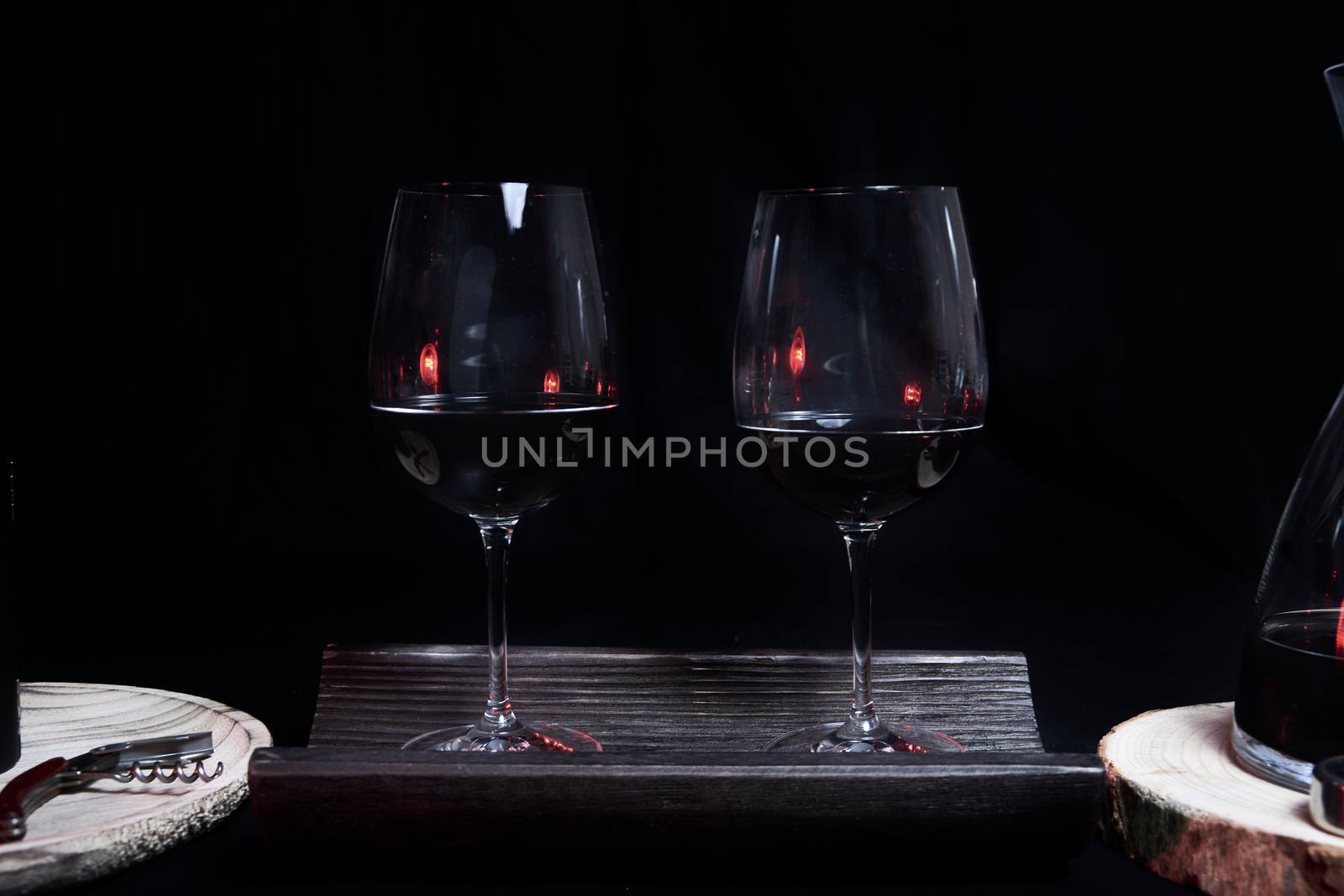 Two wine glasses filled on top of a tile, On a black background and utensils for wine