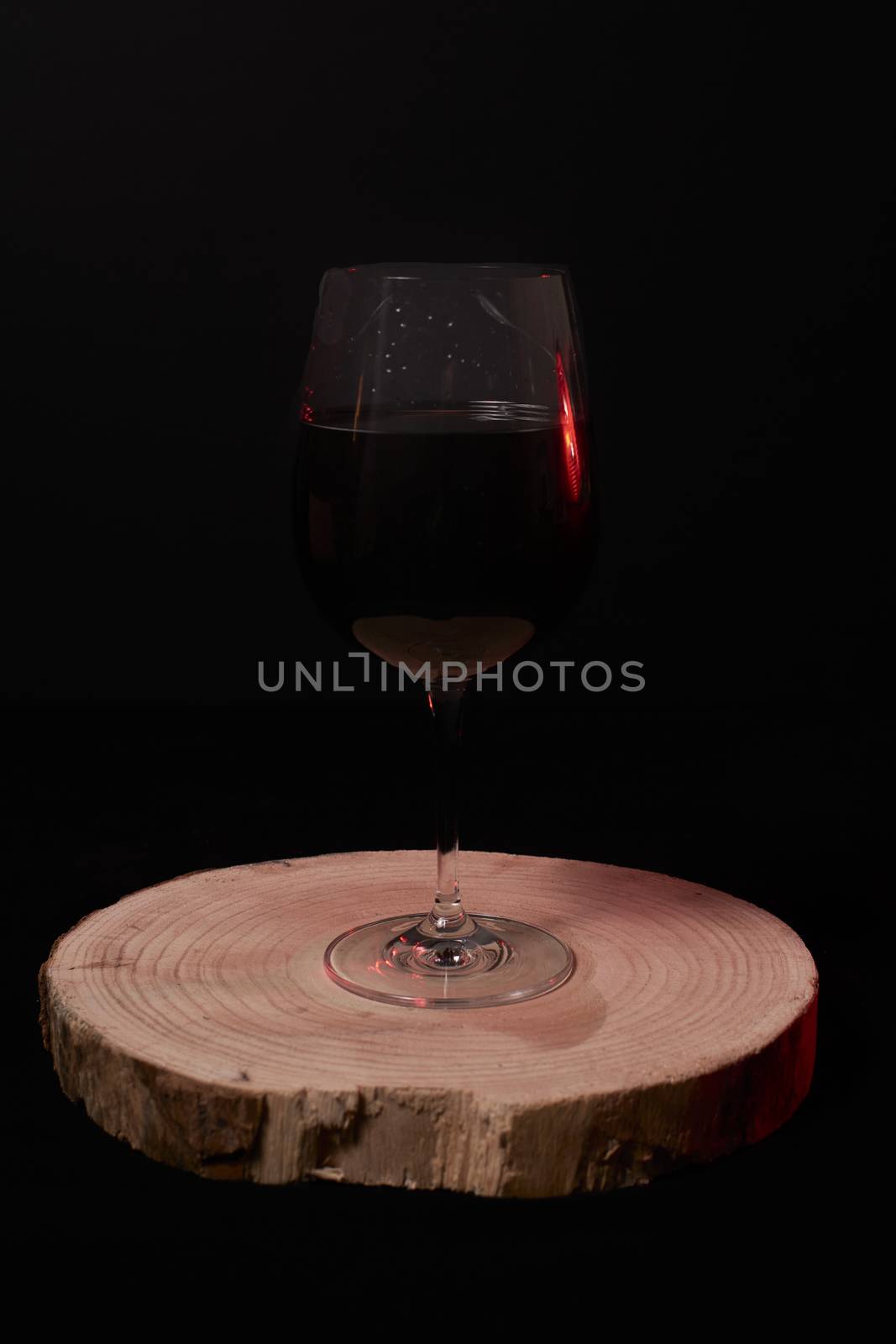 Glass of red wine on wooden stump, on black background