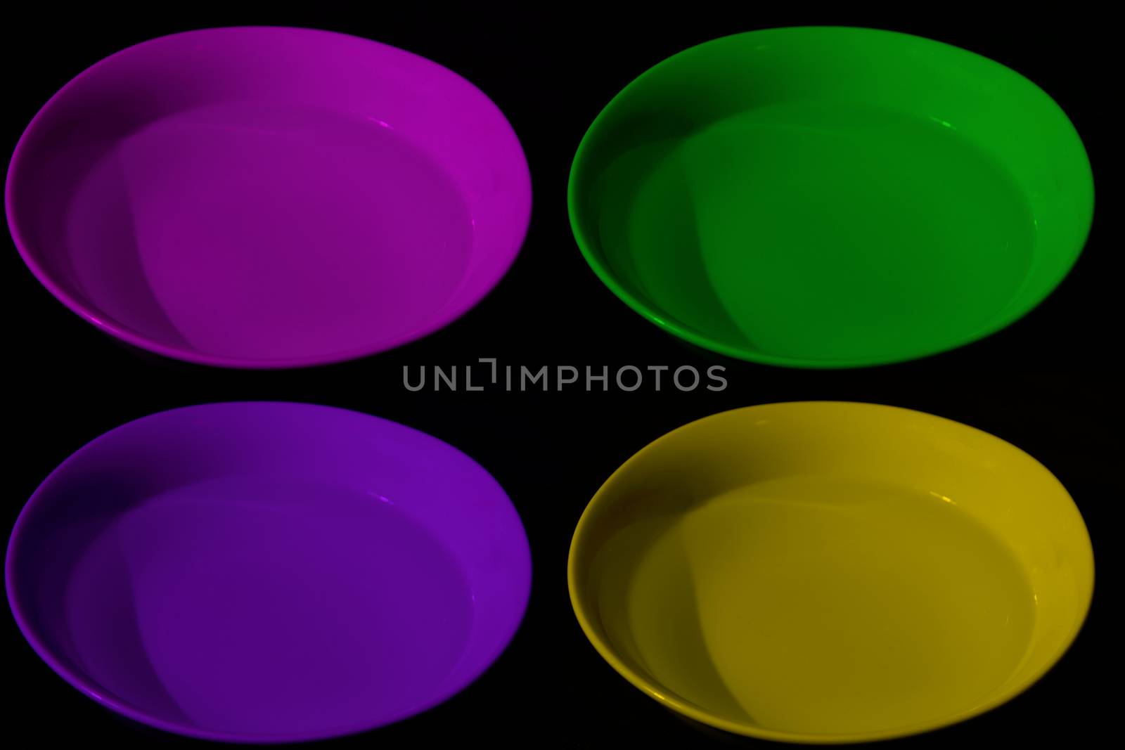 Four bowls with water of different colors, magenta, yellow, purple and green, black background, complementary colors