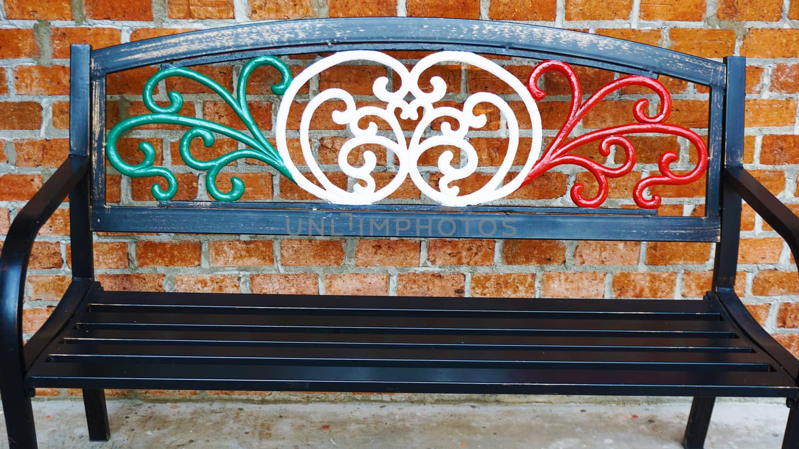 An iron bench chair draped in Italian flag colors outside of an Italian restaurant . Metal bench furniture for people waiting outside the restaurant.