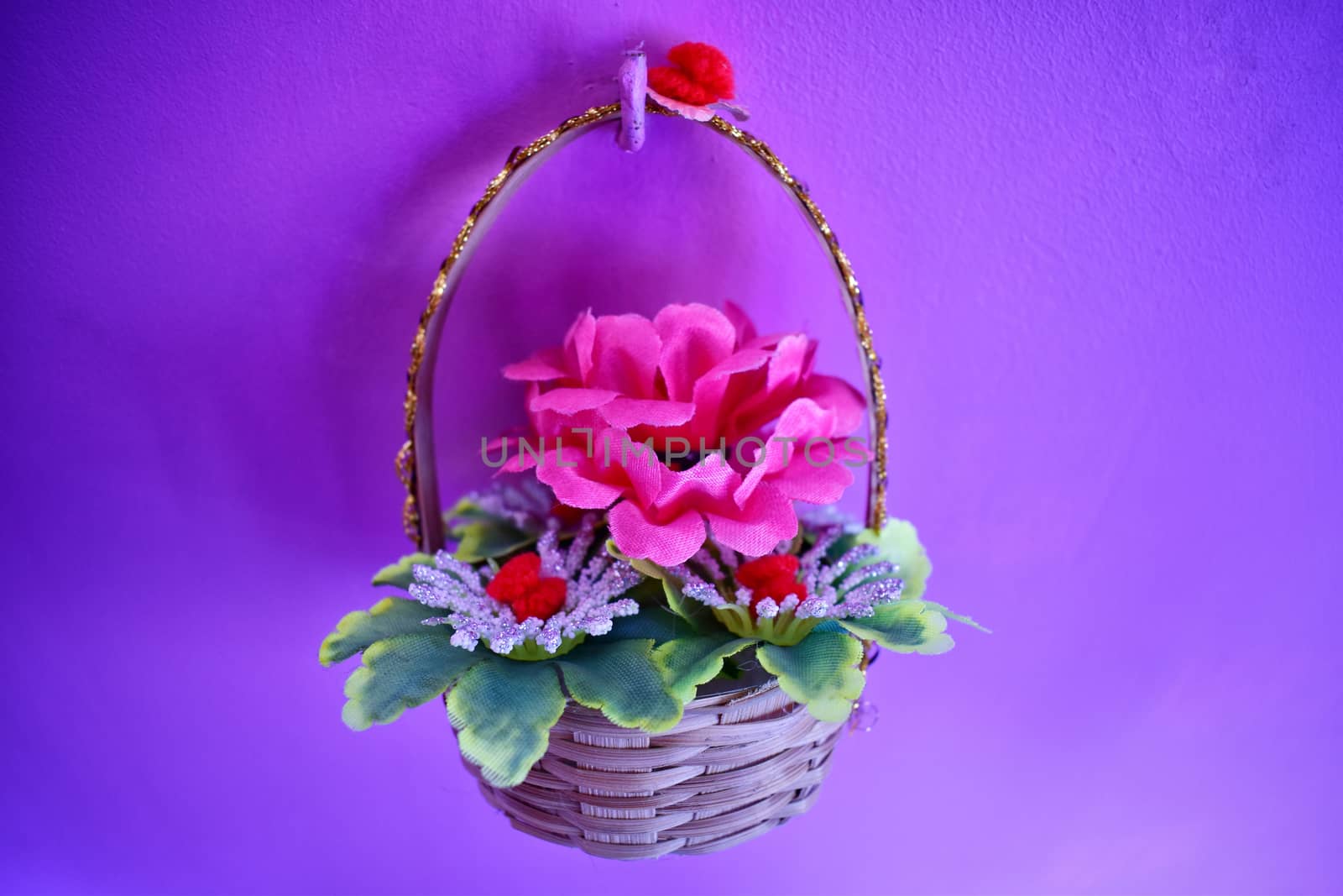 A colorful bamboo basket with artificial pink flower and green leaves