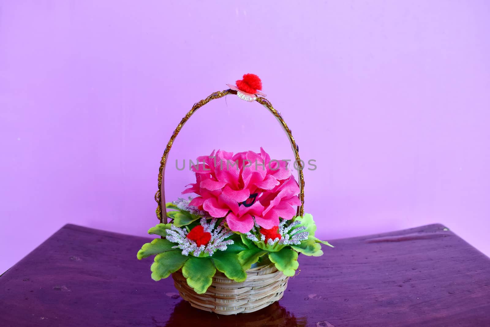 A colorful bamboo basket with artificial pink flower and green leaves
