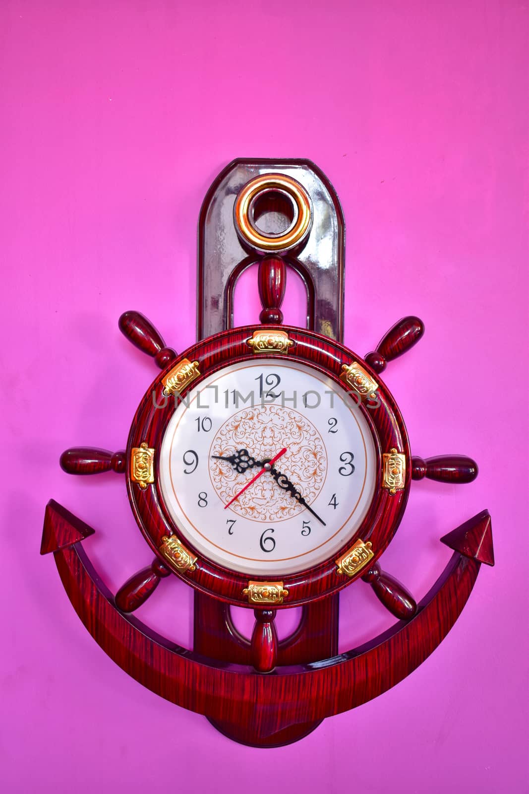 A well designed ship wheel and anchor wall clock hanging on pink wall