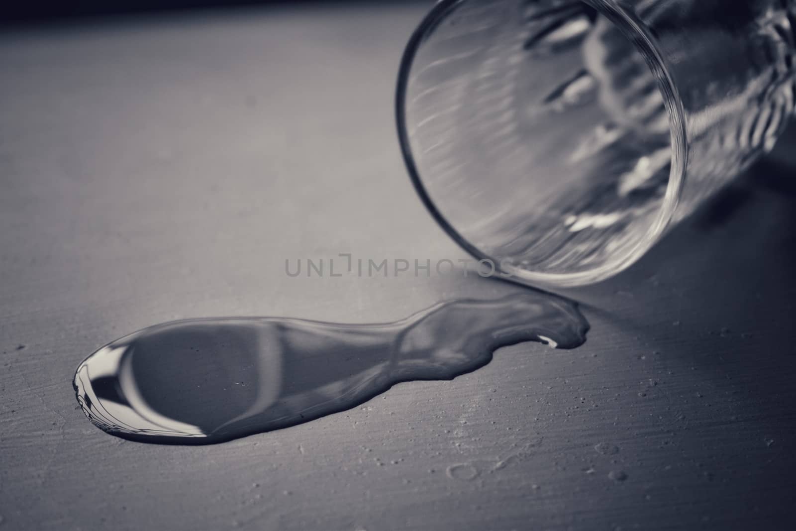 Black and white picture of pouring a little amount of water on ground from an empty glass