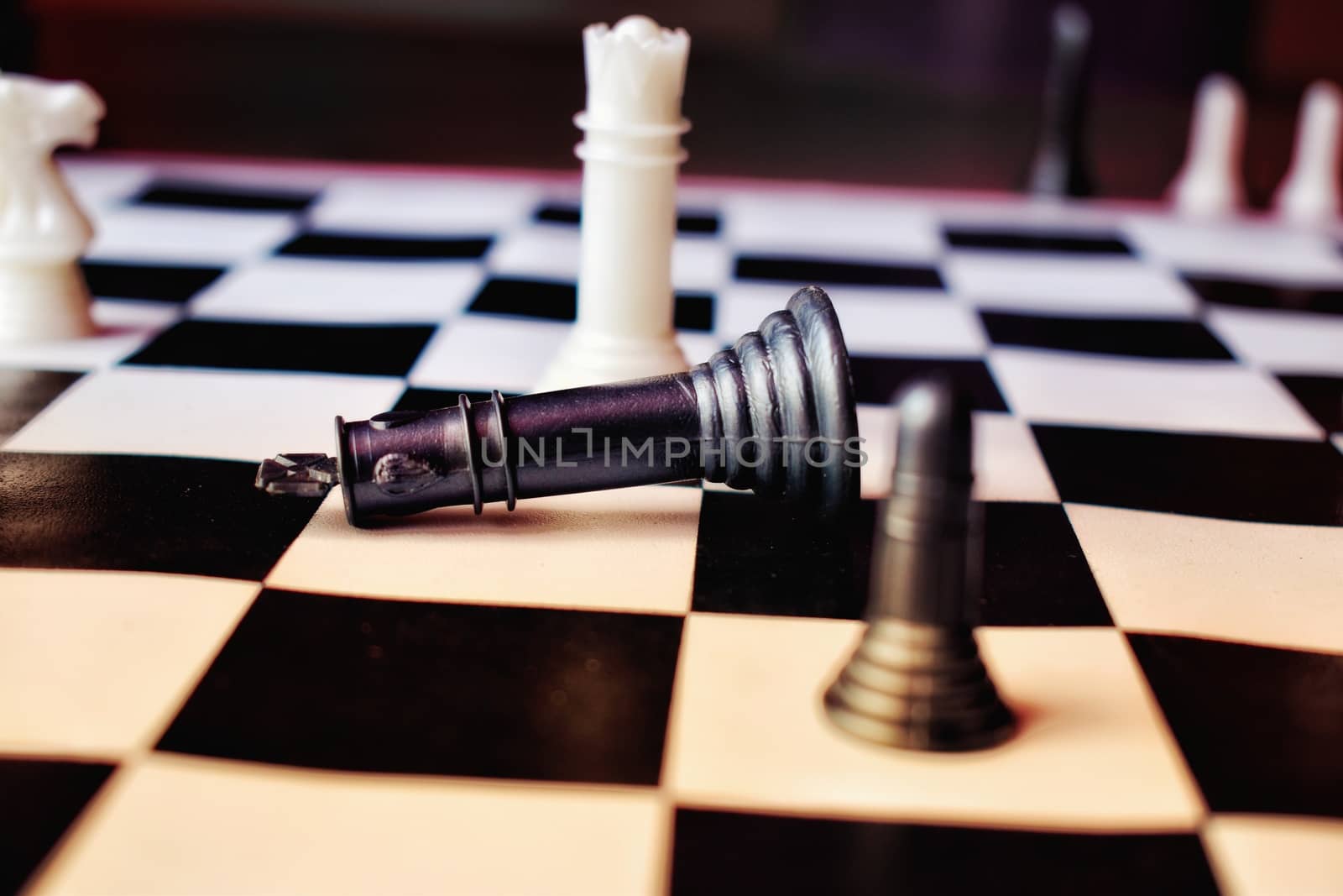 Chess game ongoing on a chess board . the black king fall down on the board.