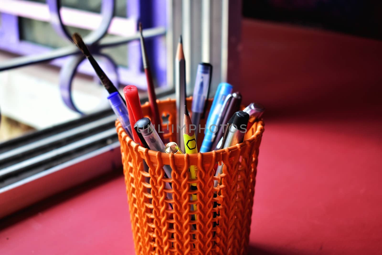 An orange colored pen case with many types of pens and pencils and some paint brush