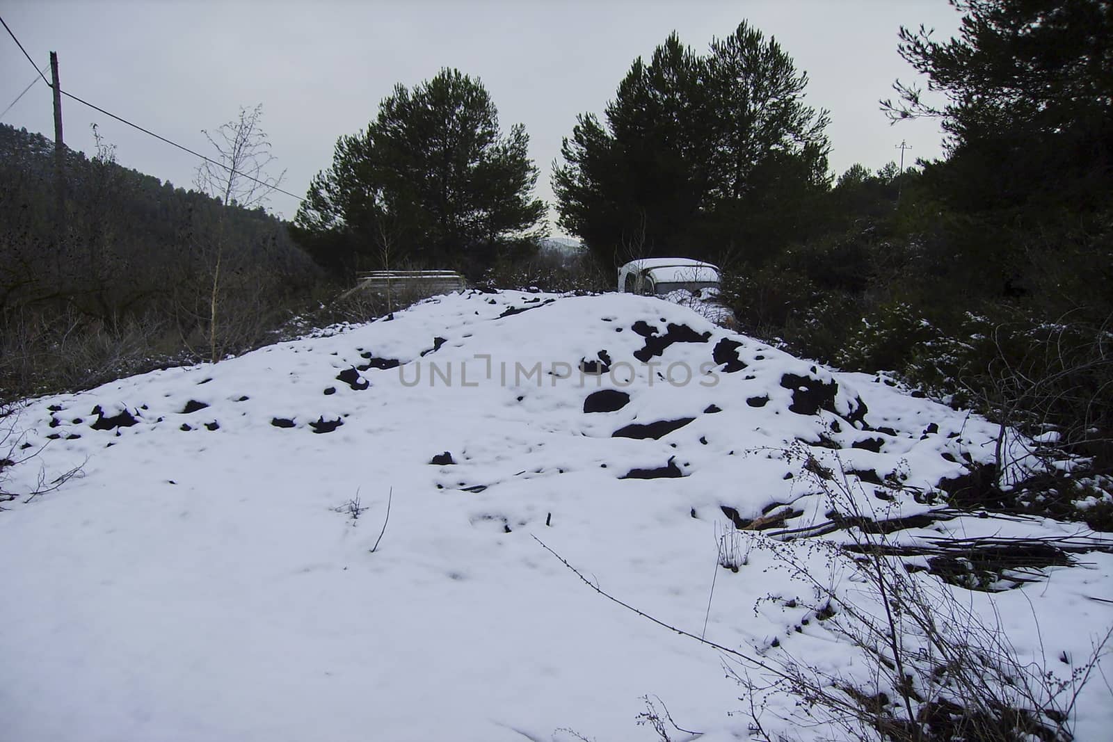 Old abandoned car in snow landscape, surrounded by trees and storm sky