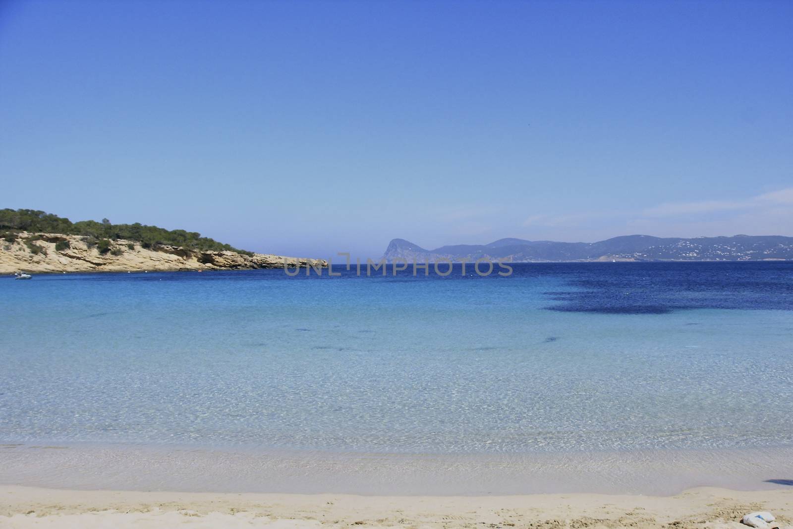 Deserted beach with turquoise waters, bright day, Mountains in the background and bright blue day