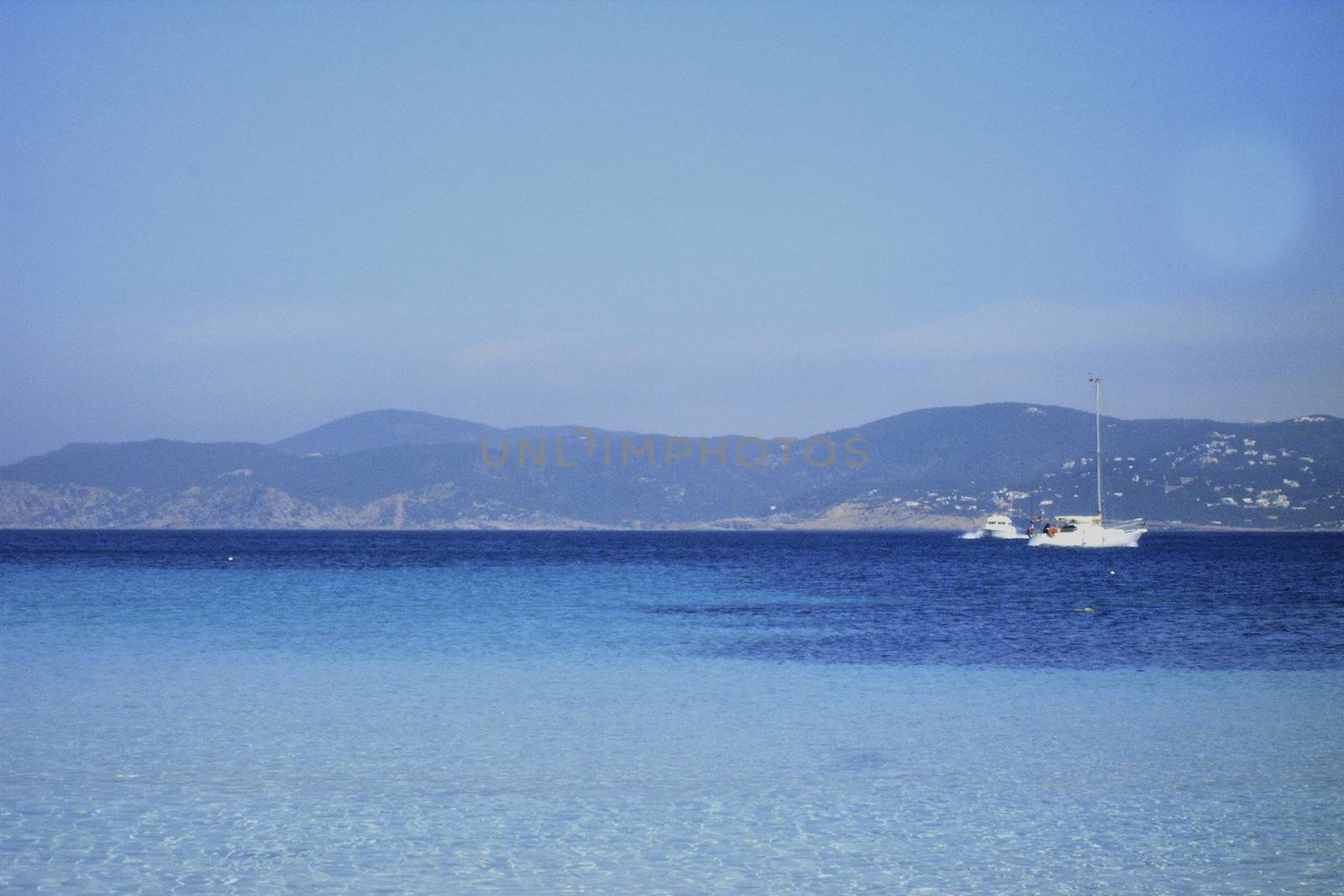 Deserted beach with turquoise waters, bright day, Mountains in the background and bright blue day, two boats sailing