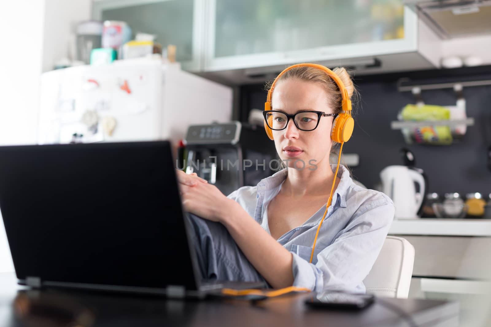 Female freelancer in her casual home clothing working remotly from her dining table in the morning. Home kitchen in the background. Stay healthy and stay at home during corona virus pandemic.