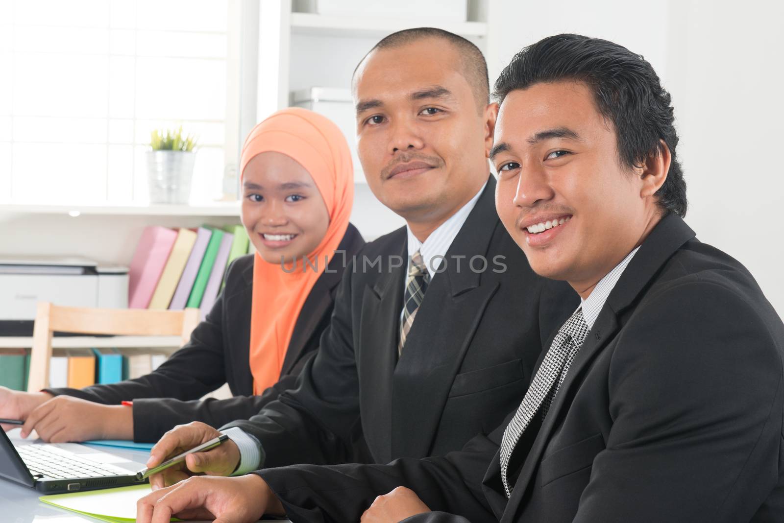 Group of Malaysian businesspeople meeting or having discussion on desk inside office room.