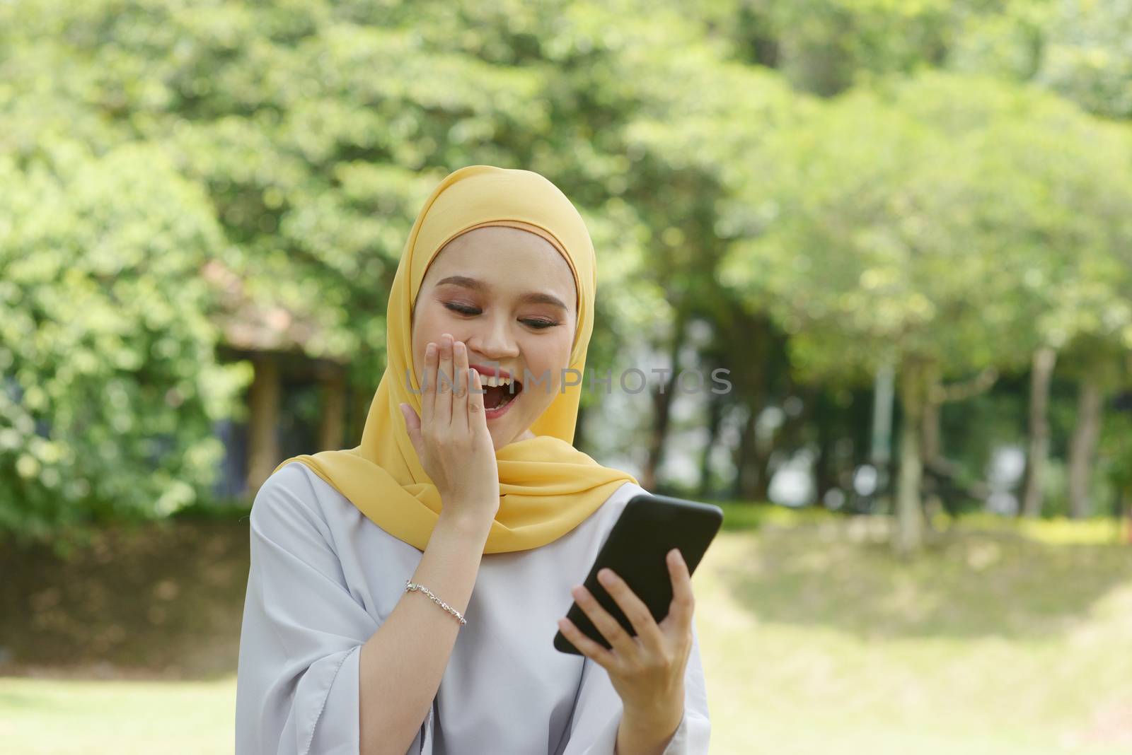 Portrait of cheerful Muslim girl using smartphone, smiling at outdoor.