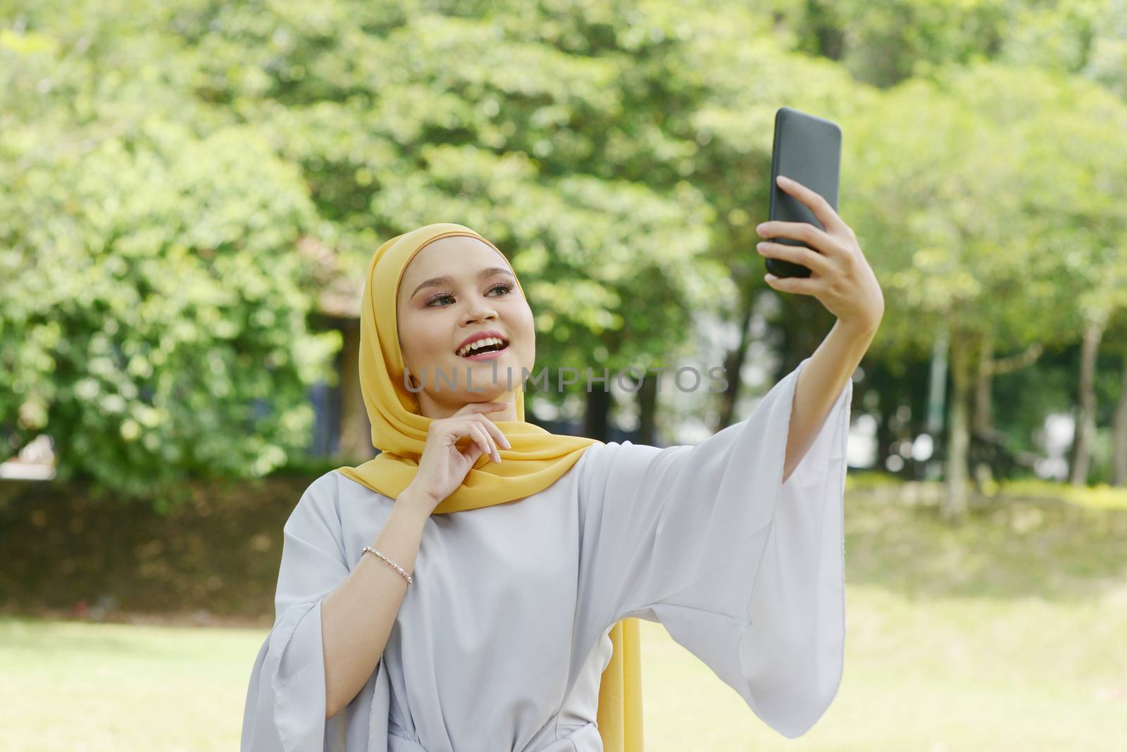 Portrait of cheerful Muslim girl using smartphone, smiling at outdoor.