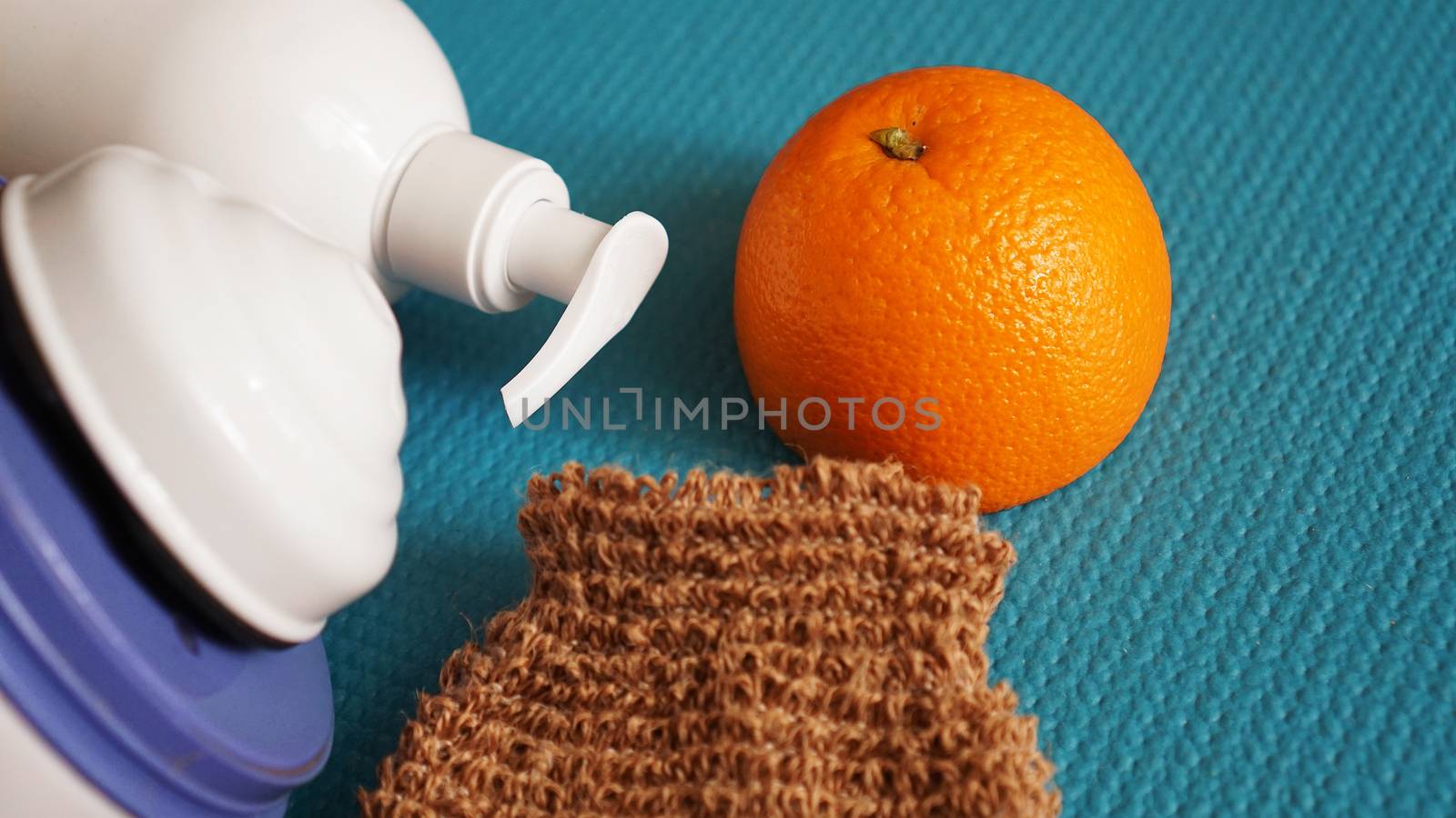 Lotion, orange, shower sponge and anti-cellulite massager on a blue background. Healthy and beautiful skin concept.