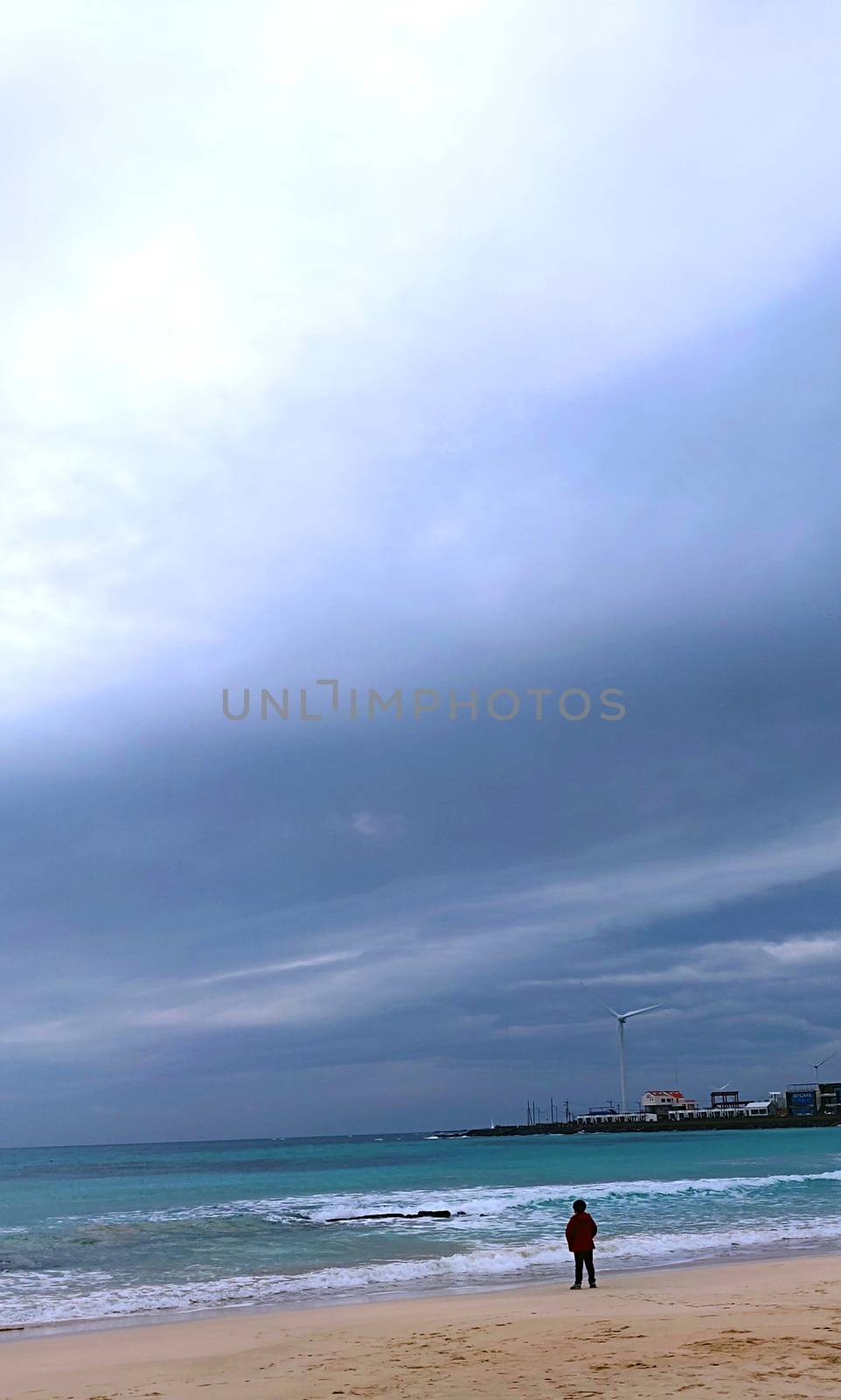 Landscape of a kid looking at the ocean and light from heavens falling on him standing on the beach in a ed sweatshirt.