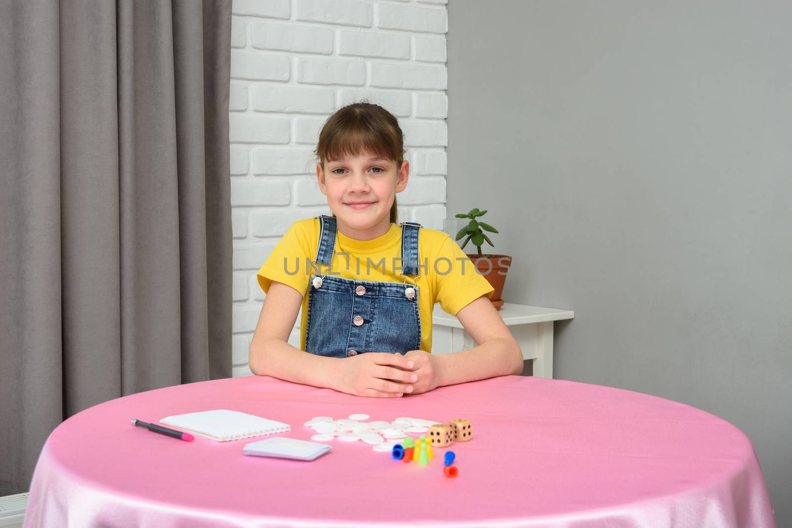 A girl sits at a table and prepares to play a board game