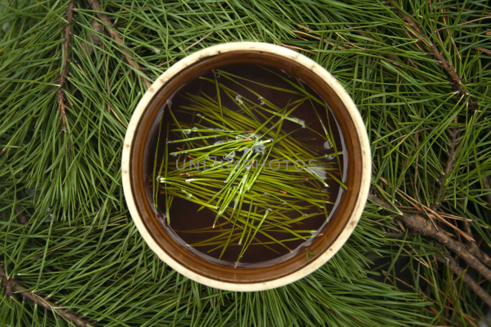 Cup of black tea with pine tree needles in it on green needles background top view. Healthy beverage tea in old cup.