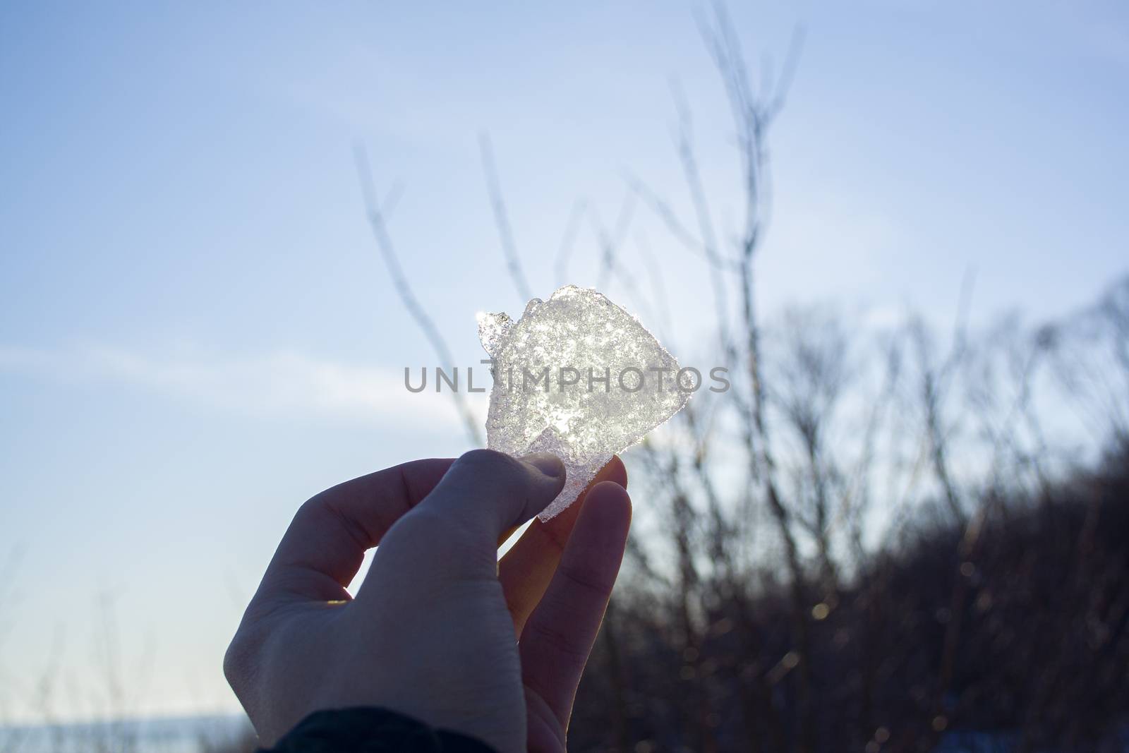 Piece of ice in man's hand close up against the sun. Look at the sun through the ice