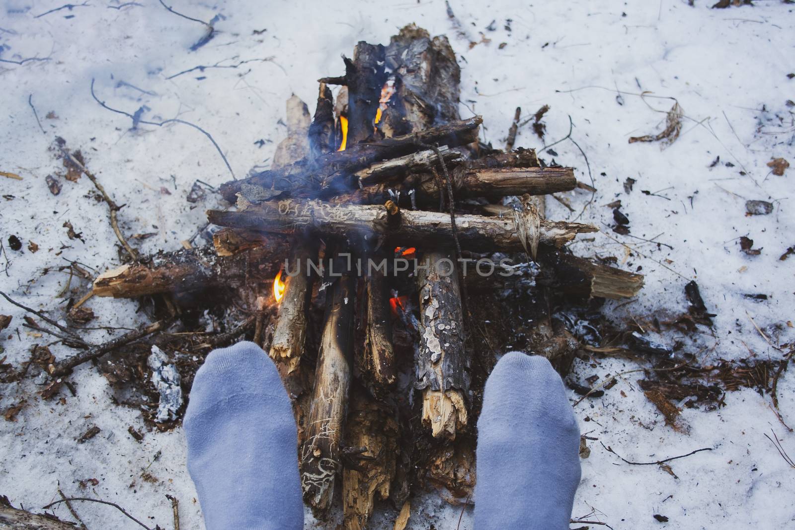 Man's legs against the bonfire in the forest. Bushcraft symbol. Solo survival in nature. Winter in the forest, travel