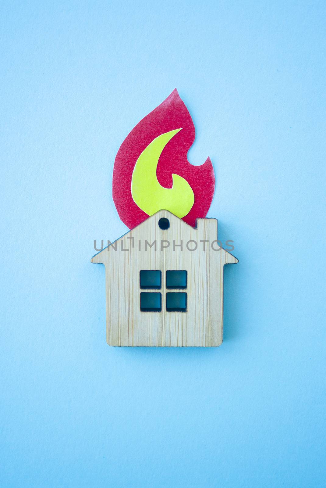 Fire house, insurance and mortgage concept. Small wooden house toy and paper fire shape on blue background top view vertical