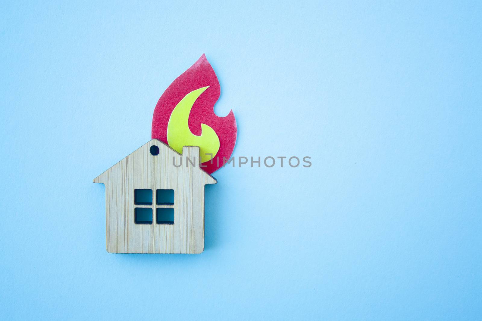 Fire house, insurance and mortgage concept. Small wooden house toy and paper fire shape on blue background top view with copy space