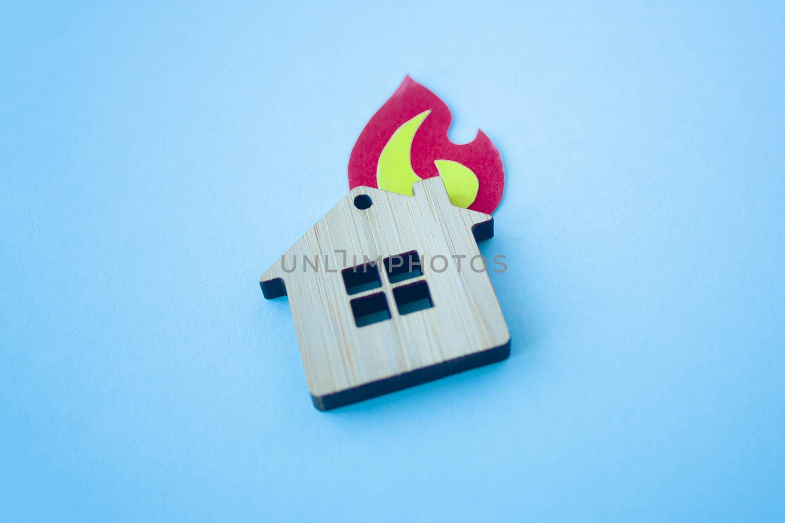 Fire house, insurance and mortgage concept. Small wooden house toy and paper fire shape on blue background side view with copy space