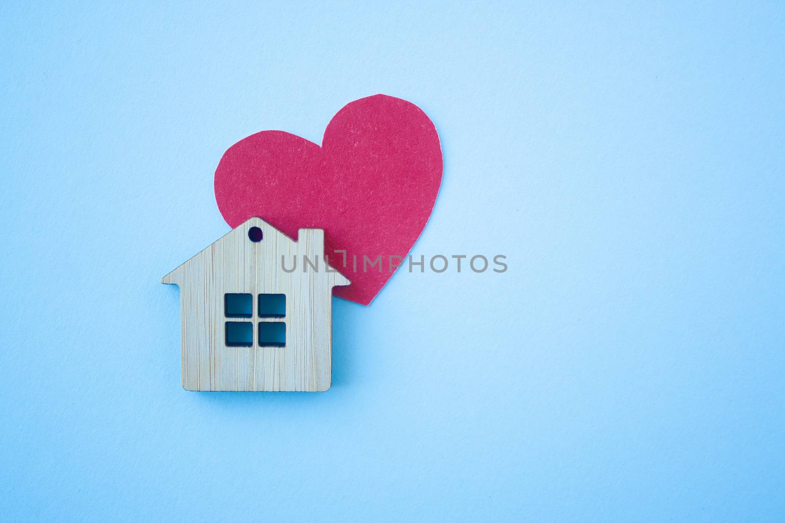 Love home, insurance and mortgage, marriage and valentine concept. Small wooden house toy and paper heart shape on blue background top view copyspace