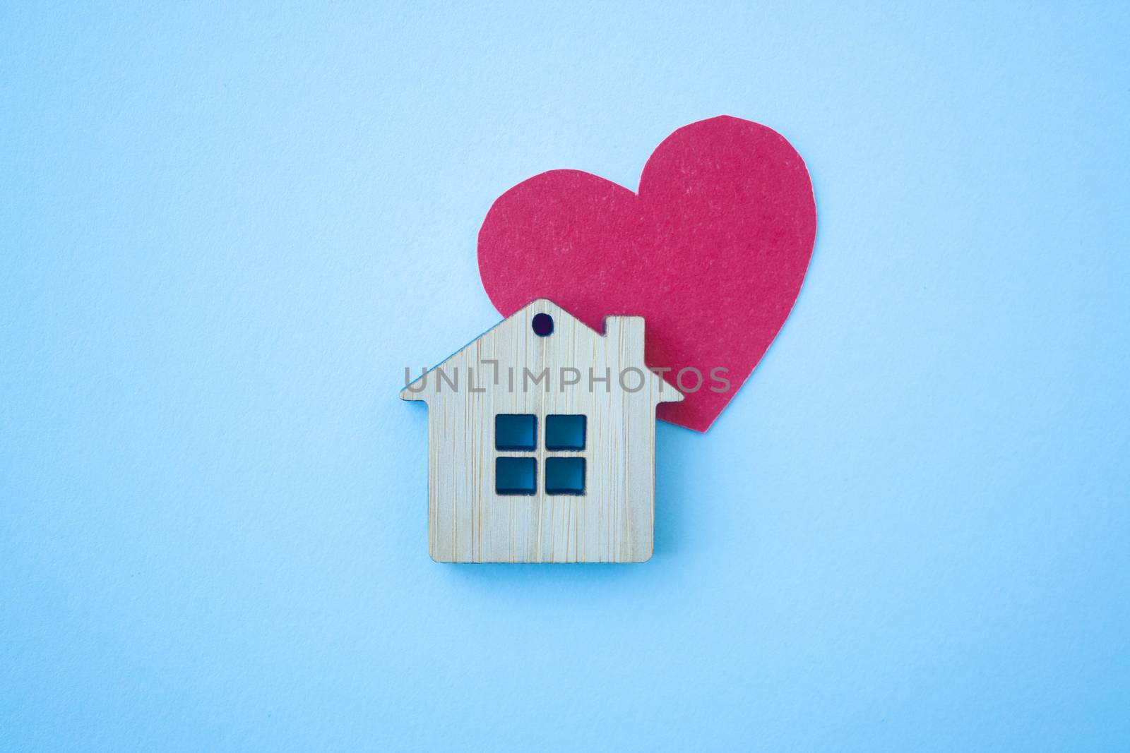 Love home, insurance and mortgage, marriage and valentine concept. Small wooden house toy and paper heart shape on blue background top view 