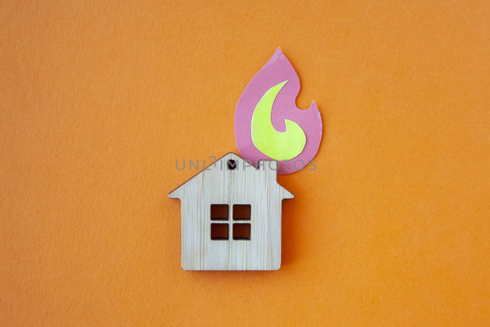 Fire house, insurance and mortgage concept. Small wooden house toy and paper fire shape on orange background top view