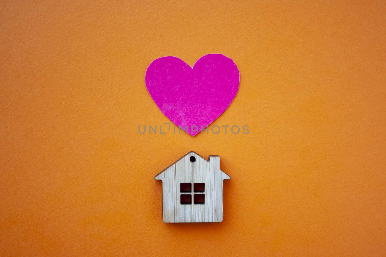 Love home, insurance and mortgage, marriage and valentine concept. Small wooden house toy and paper heart shape on orange background top view 