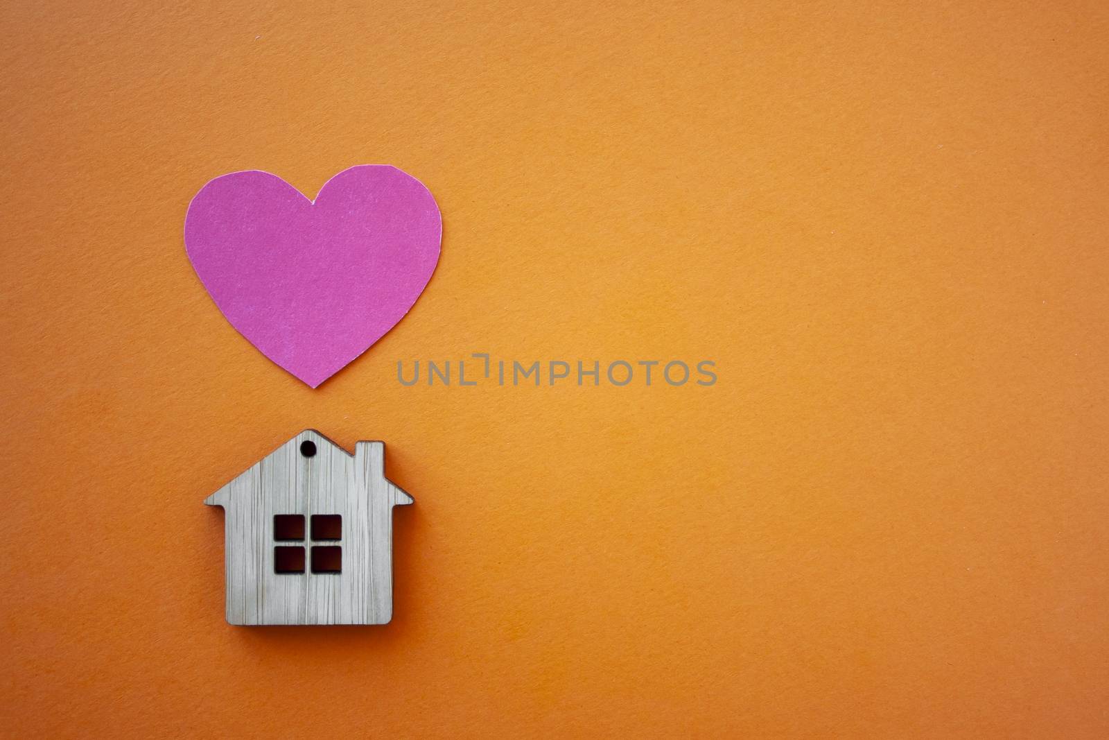 Love home, insurance and mortgage, marriage and valentine concept. Small wooden house toy and paper heart shape on orange background top view copyspace