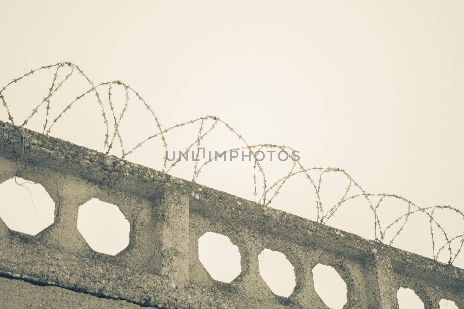 Barbed wires at stone fence on cloudy sky, security, prison concept. 