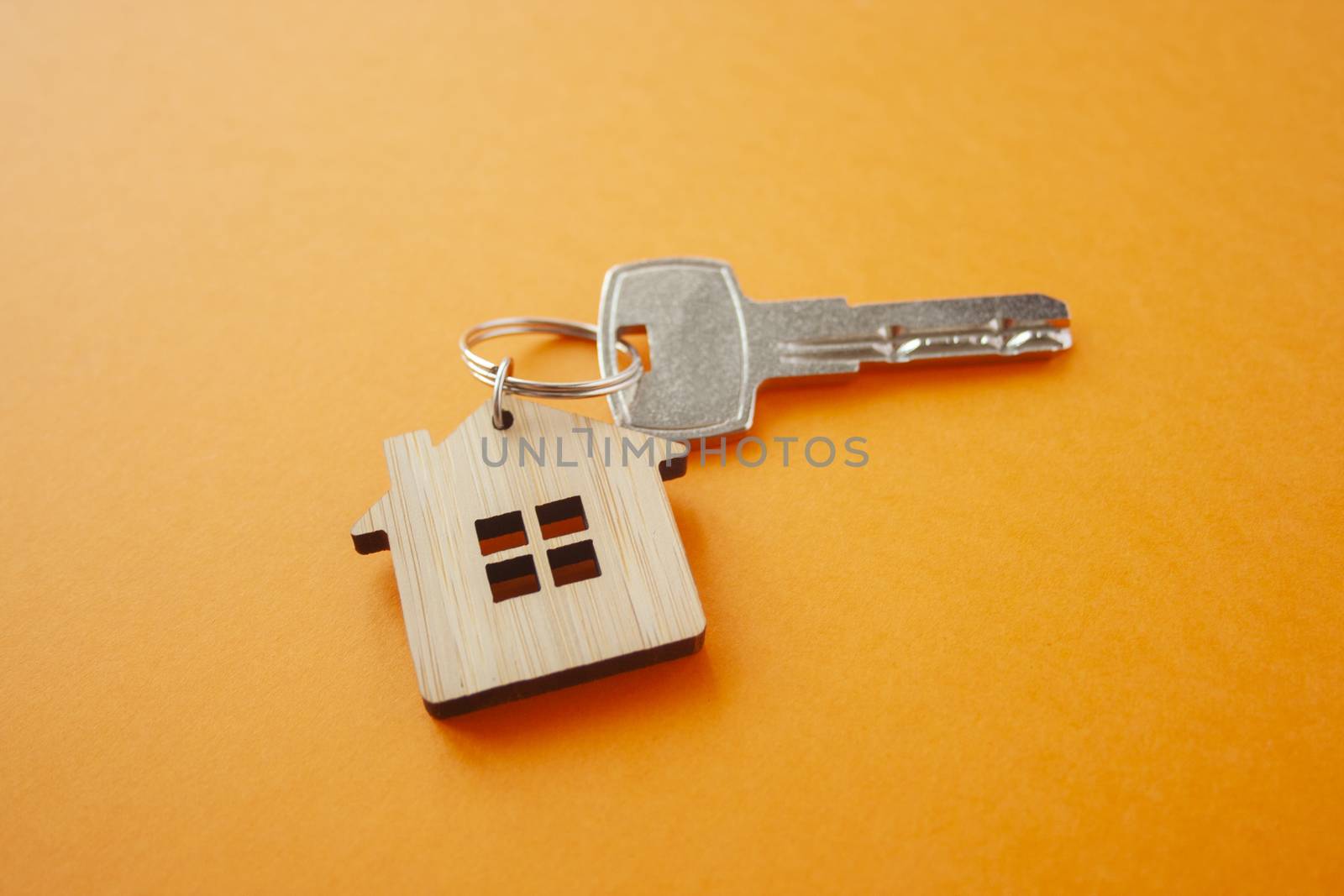 Key and house shaped keychain arrangement on orange background. Top view, flat lay. Real estate, insurance concept, mortgage, buy sell house, realtor concept
