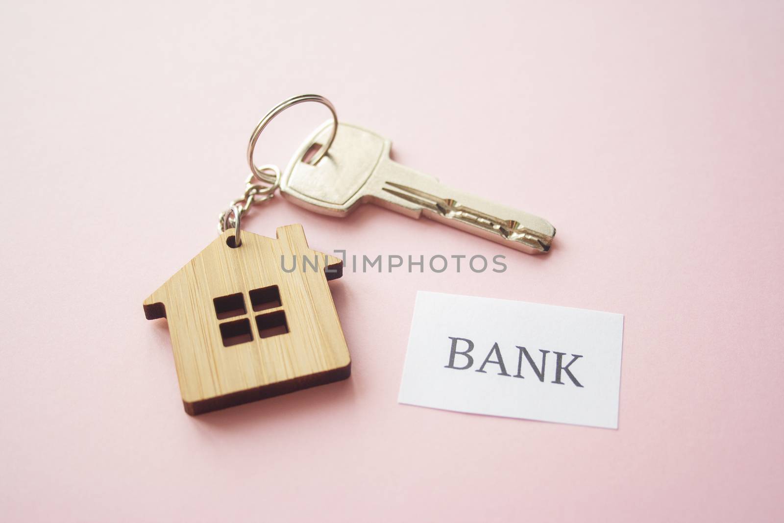 Wooden house toy and silver key on bright pink background with phrase quote Bank. Mortgage, house buy sell, investment, rent, realtor concept