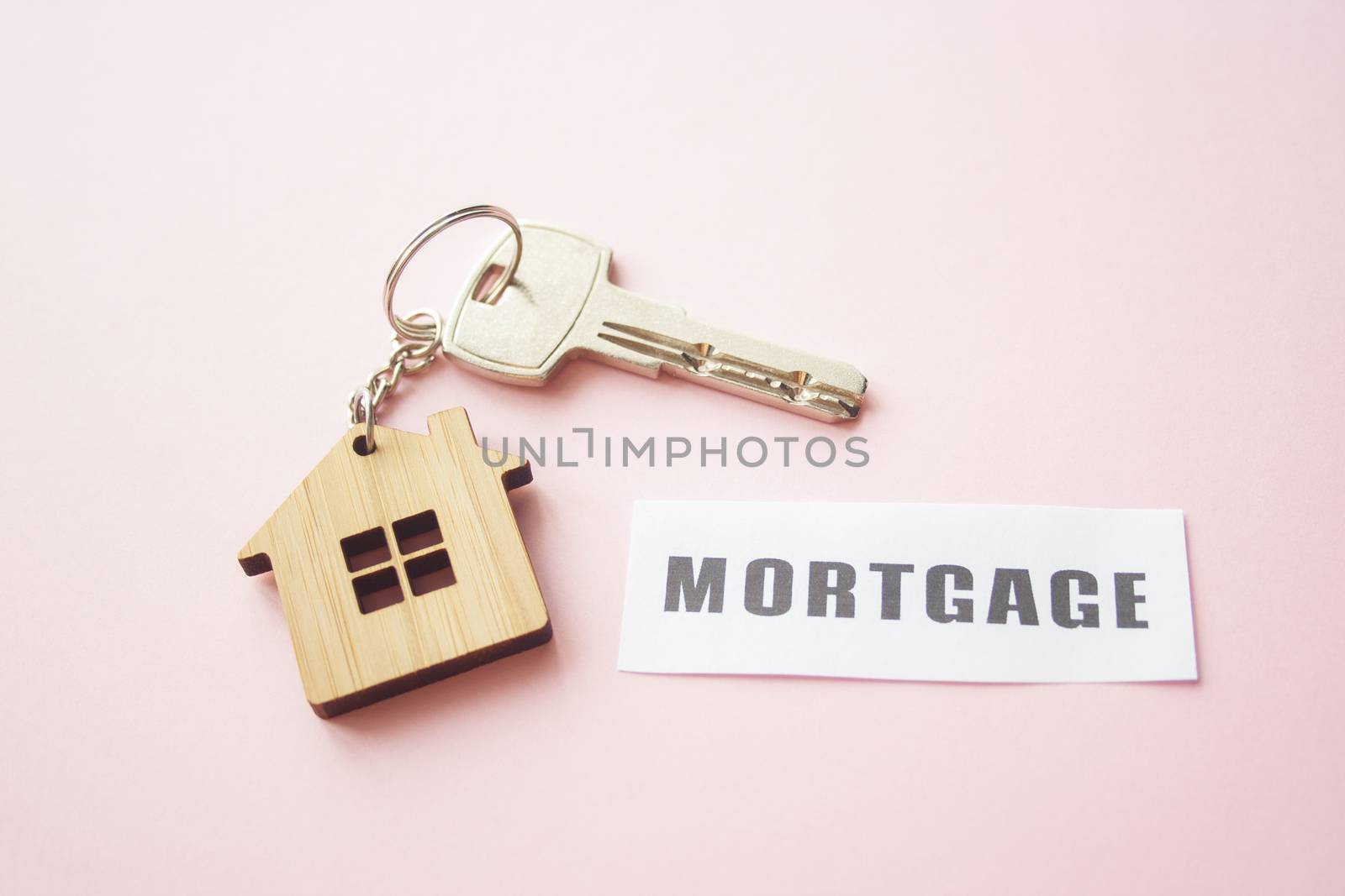 Wooden house toy and silver key on bright pink background with phrase quote Mortgage. Mortgage, house buy sell, investment, rent, realtor concept