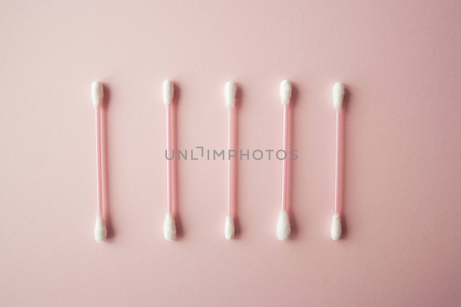 Flat lay cotton buds on pink warm background. Row of cotton swubs, beauty and health care concept. Cotton composition