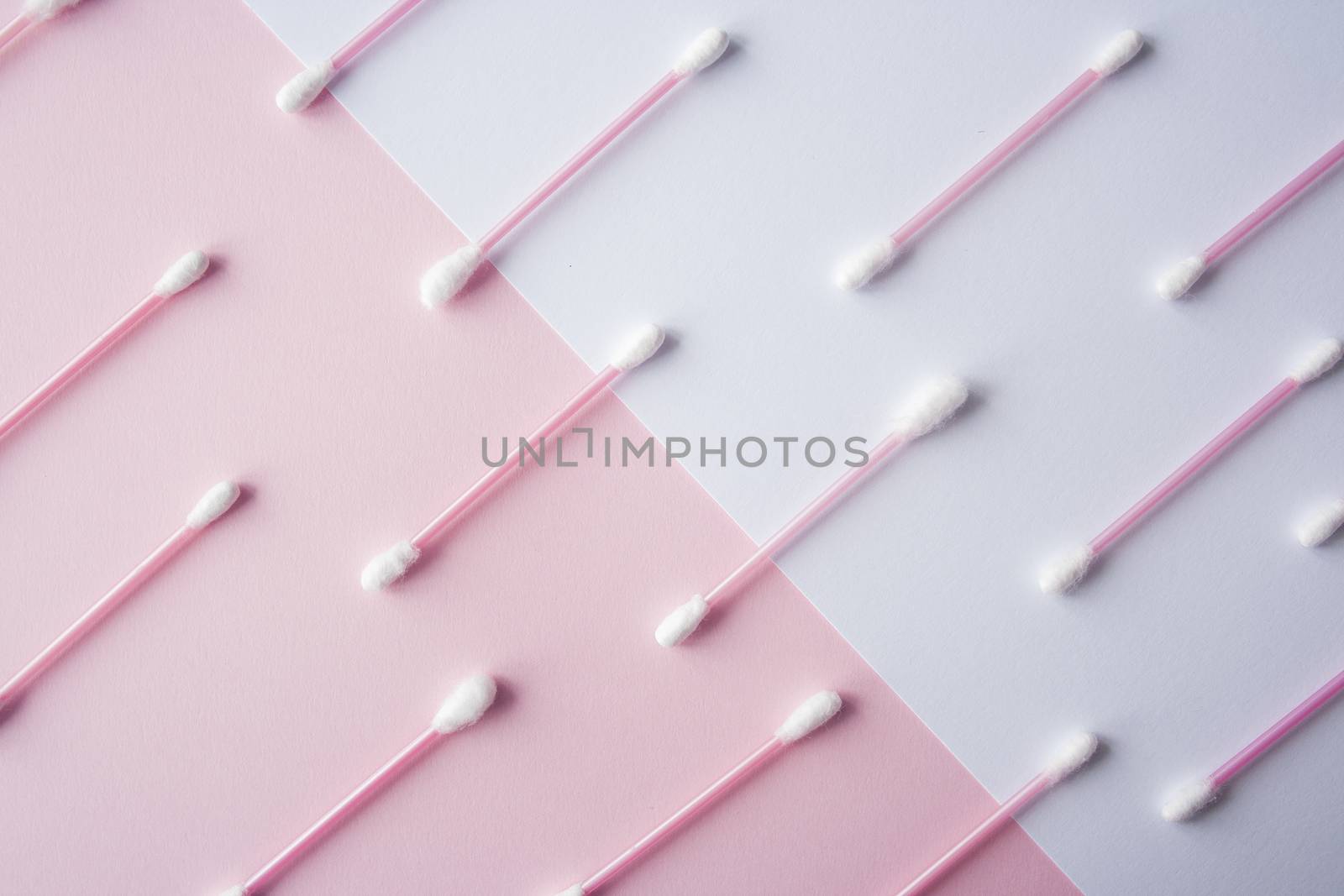 Flat lay cotton buds on pink warm and blue background. Pattern of cotton swubs, beauty and health care concept. Cotton composition