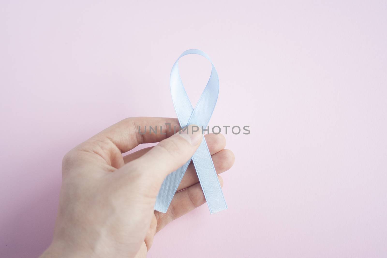 November Prostate Cancer Awareness month, Man Hand holding Blue Ribbon  on pink background for people living and illness. Cancer awareness