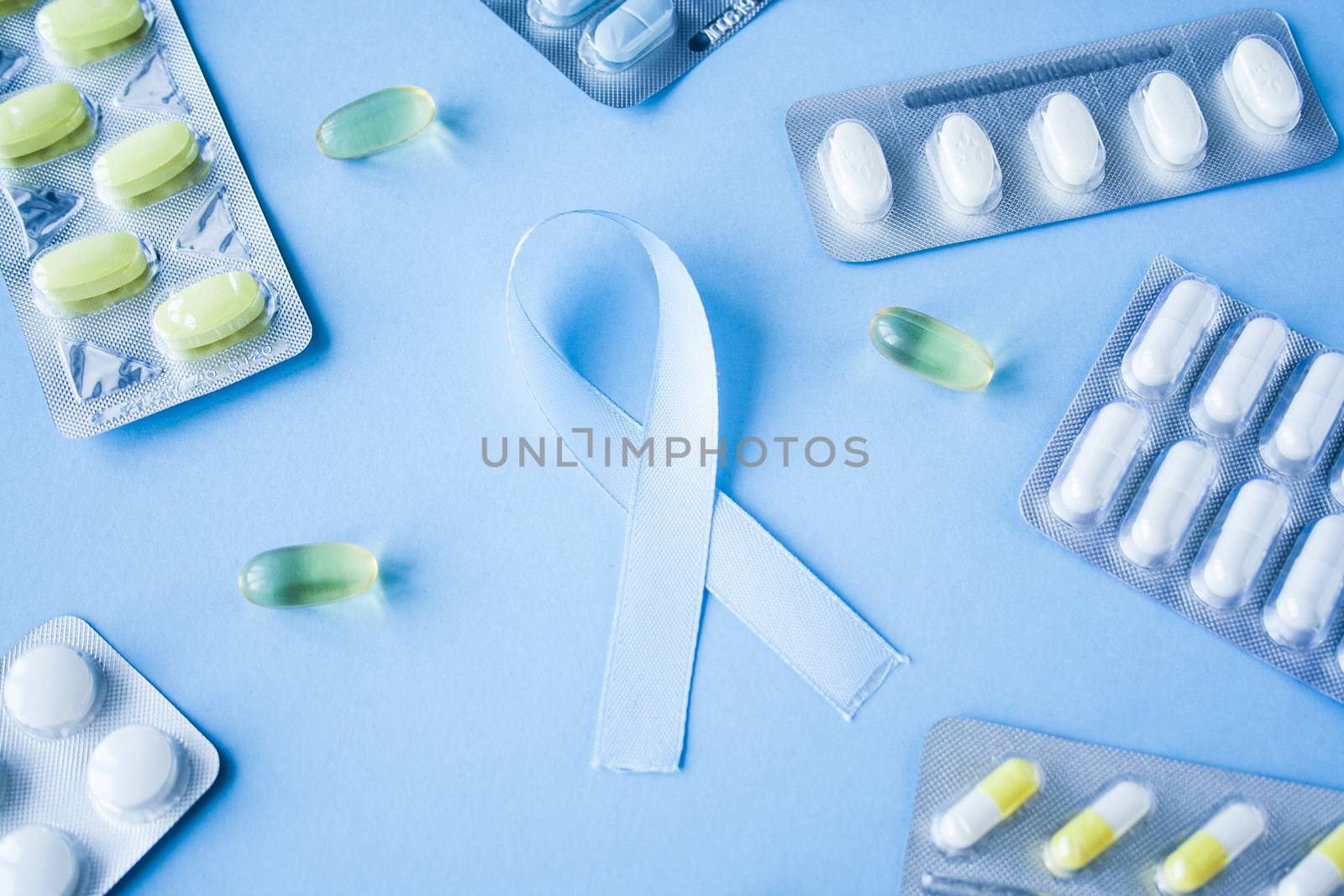 Blue ribbon symbol of prostate cancer with many pills and drugs clusters on bright background. Cancer awareness, cure, treatment concept. Oncology and carcinoma, ribbon