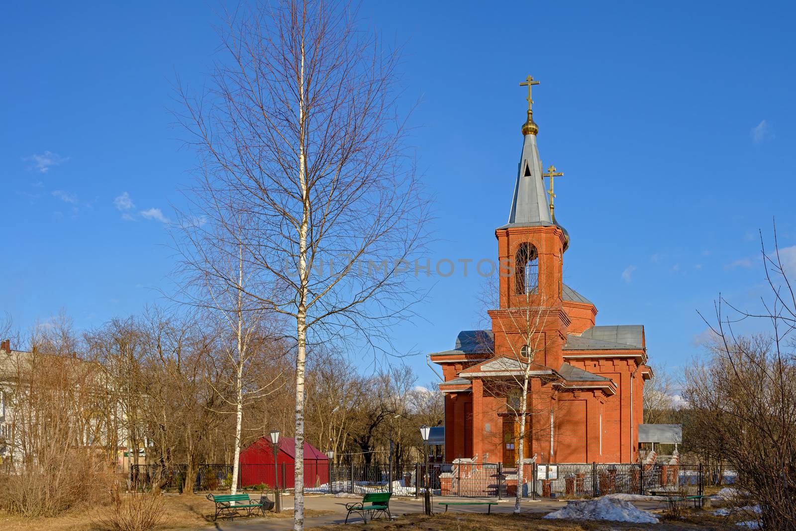 Orthodox church of red brick surrounded by trees under a blue sky in spring. by vladali