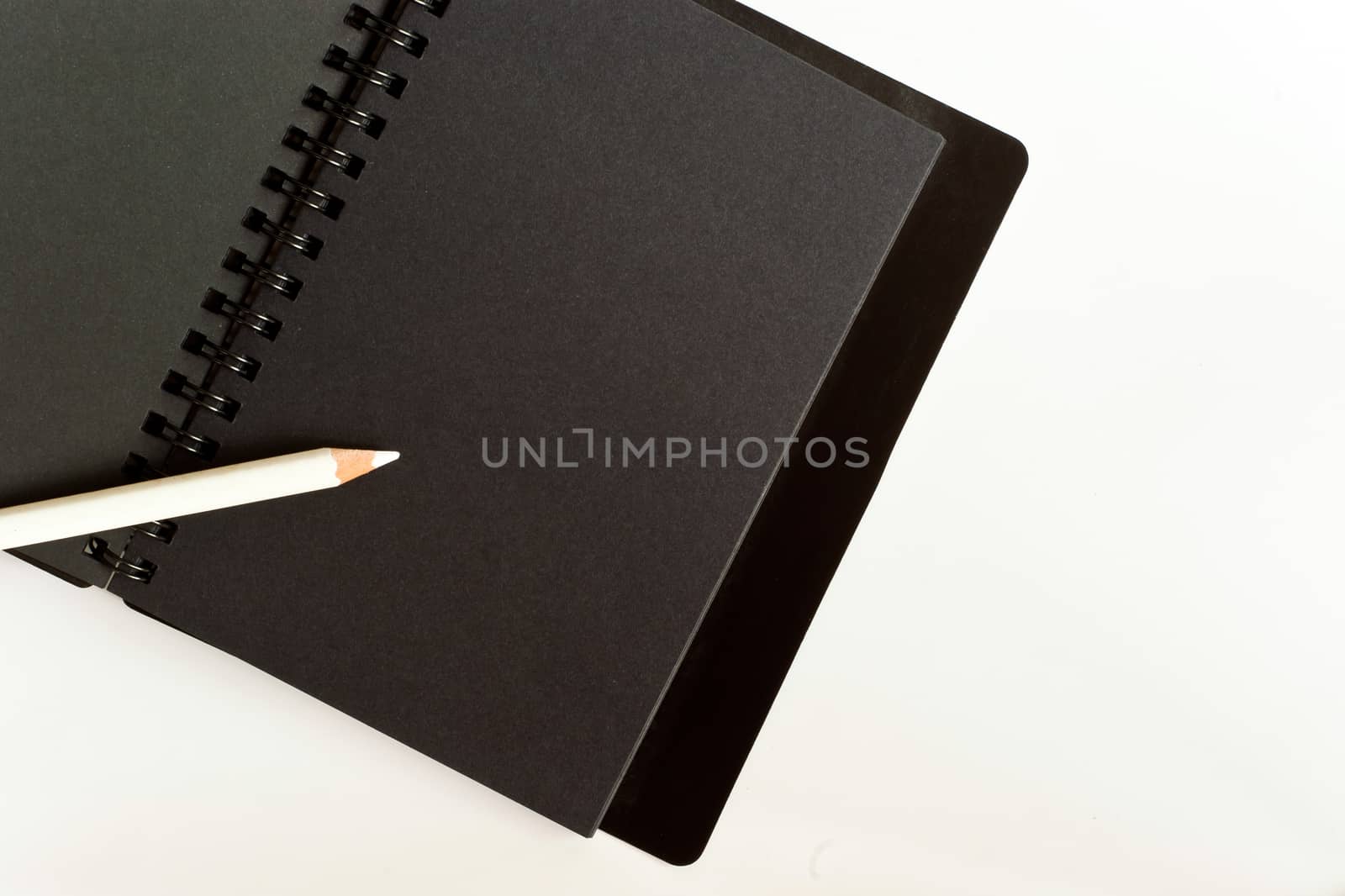 Black paper spiral notebook and white pencil by Satakorn
