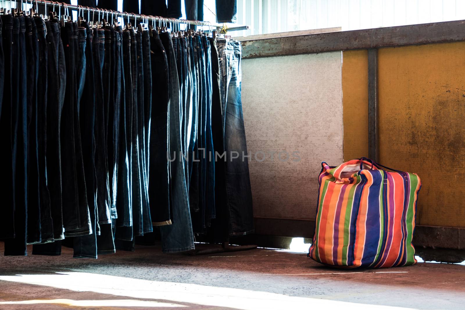 Multi color on Plastic sack and the row of denim pants hanging on trempels. Jeans in clothing store