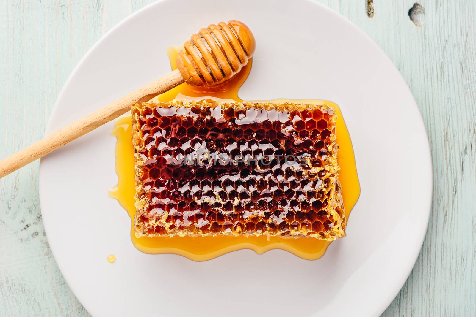 Honeycomb on white plate with honey dipper by Seva_blsv