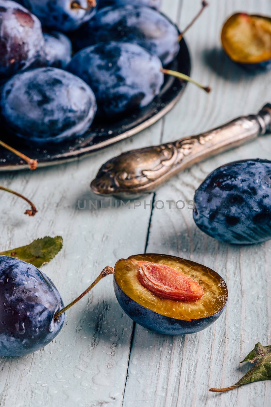 Ripe plums with sliced fruits, leaves and vintage knife over light wooden surface