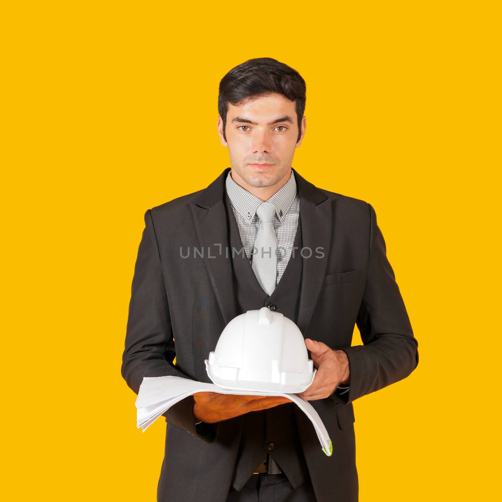 Young businessman in a gray shirt and black suit holding a white construction hat and the construction drawings. The concept of investing in good business. Portrait with studio light.