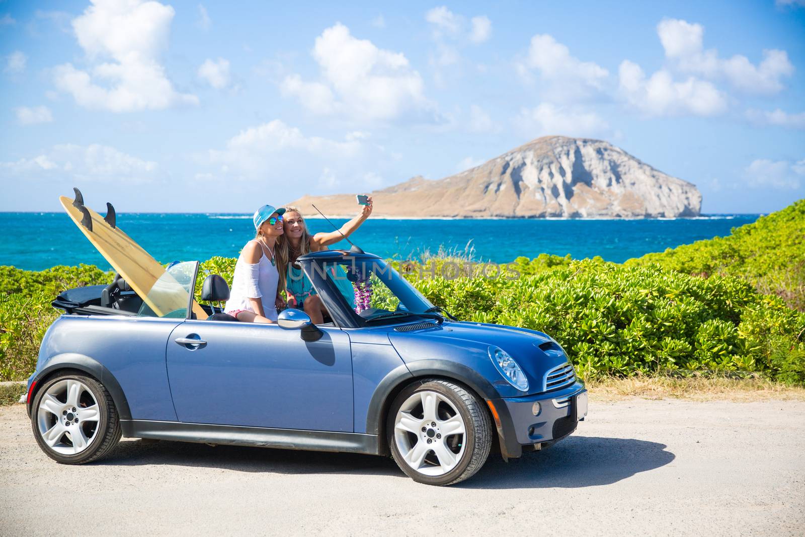 Car road trip vacation young people taking selfie photo with phone during summer travel vacation. Tourists couple taking photos on Hawaii in convertible car, with smartphone camera