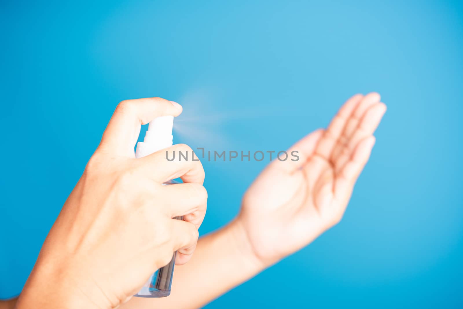 Closeup Hand Asian young woman applying spray pump dispenser sanitizer alcohol on hand wash cleaning, hygiene prevention COVID-19 or coronavirus protection concept, isolated on blue background