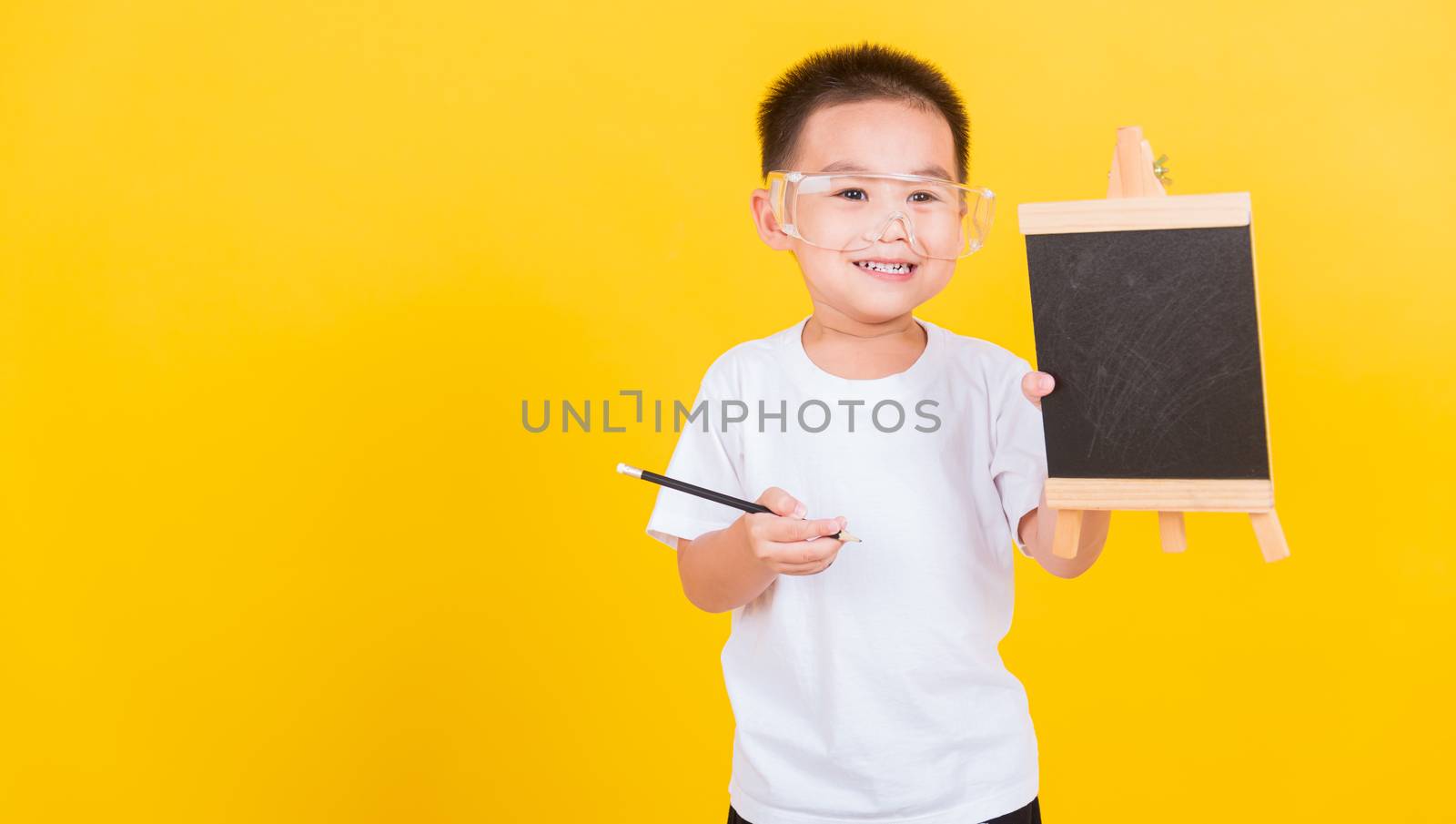 Asian Thai happy portrait cute little cheerful child boy smile he showing blackboard and looking to camera, studio shot isolated on yellow background with copy space